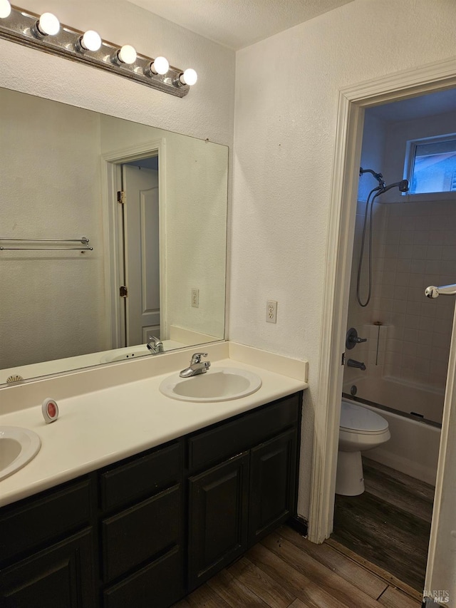 full bath with double vanity, shower / bath combination, toilet, a sink, and wood finished floors