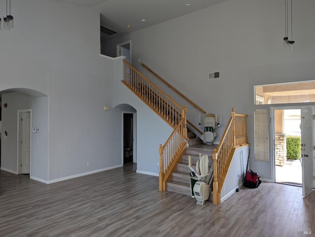 unfurnished living room featuring light wood-type flooring, arched walkways, a high ceiling, and stairs