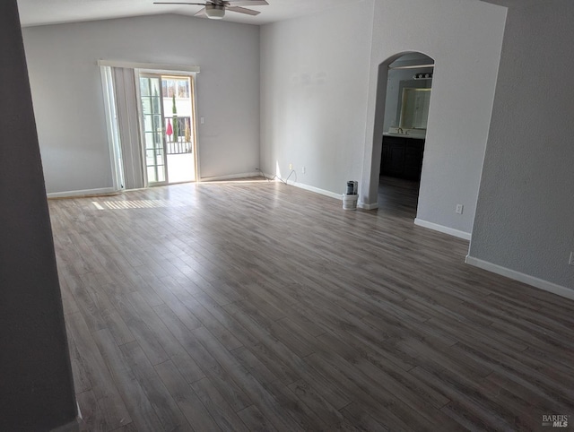 empty room featuring a ceiling fan, baseboards, arched walkways, and dark wood-style flooring