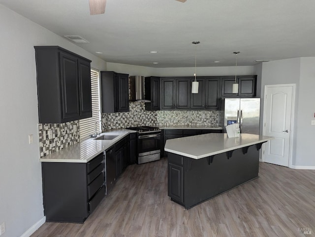 kitchen featuring a sink, hanging light fixtures, wall chimney range hood, appliances with stainless steel finishes, and light countertops