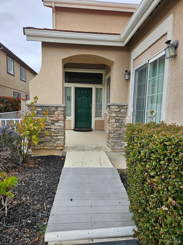 property entrance with stone siding, fence, and stucco siding