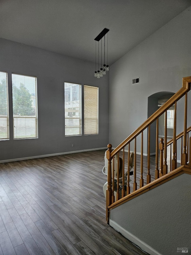 interior space featuring arched walkways, stairway, vaulted ceiling, wood finished floors, and baseboards