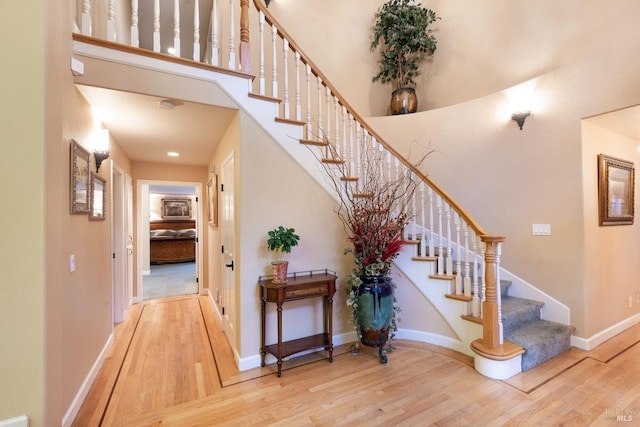 stairway with baseboards, wood finished floors, and a towering ceiling