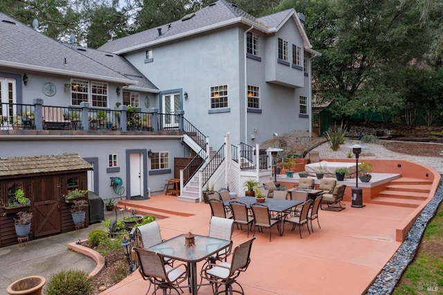 back of house featuring stairs, roof with shingles, stucco siding, a patio, and outdoor dining space