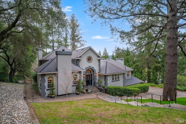 view of front of home with stucco siding, a chimney, a shingled roof, and a front lawn