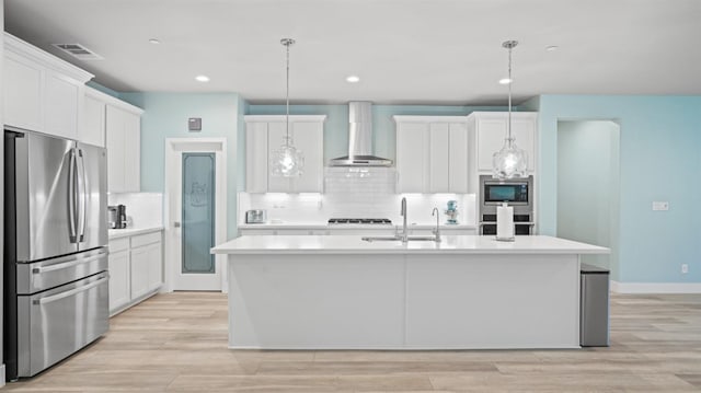 kitchen featuring a sink, white cabinets, light countertops, appliances with stainless steel finishes, and wall chimney range hood