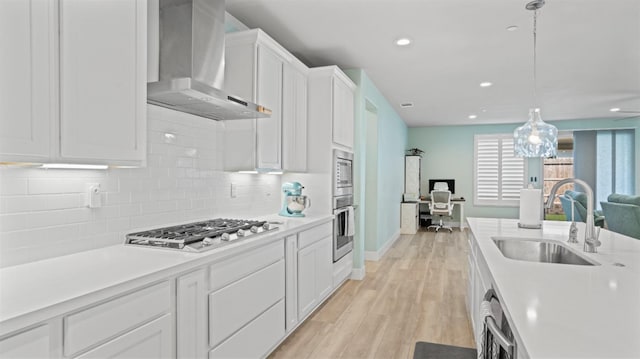 kitchen with a sink, white cabinetry, open floor plan, appliances with stainless steel finishes, and wall chimney exhaust hood