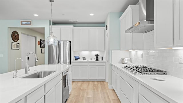 kitchen featuring visible vents, appliances with stainless steel finishes, light wood-type flooring, wall chimney range hood, and a sink