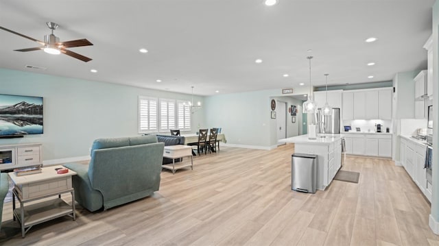 kitchen featuring light wood-style floors, open floor plan, light countertops, hanging light fixtures, and a center island with sink