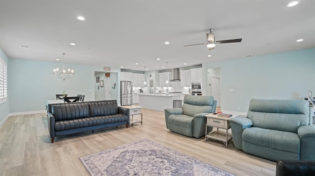 living room featuring recessed lighting, light wood-style flooring, baseboards, and ceiling fan with notable chandelier