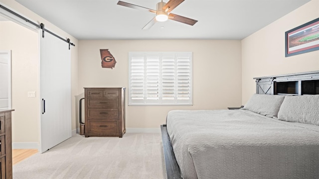 bedroom with light carpet, a barn door, a ceiling fan, and baseboards