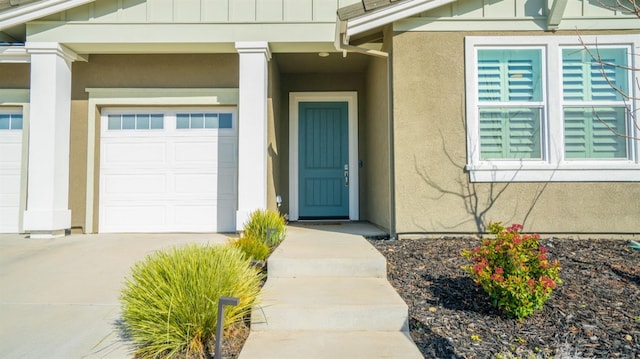 property entrance featuring a garage, concrete driveway, board and batten siding, and stucco siding