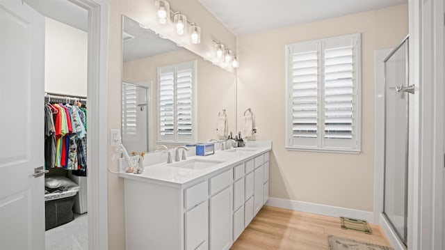 bathroom featuring double vanity, a stall shower, a sink, wood finished floors, and baseboards