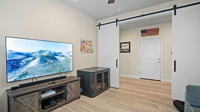 living room featuring light wood-type flooring, a barn door, baseboards, and ceiling fan