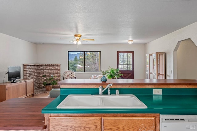 kitchen featuring a center island with sink, sink, dishwasher, and a textured ceiling