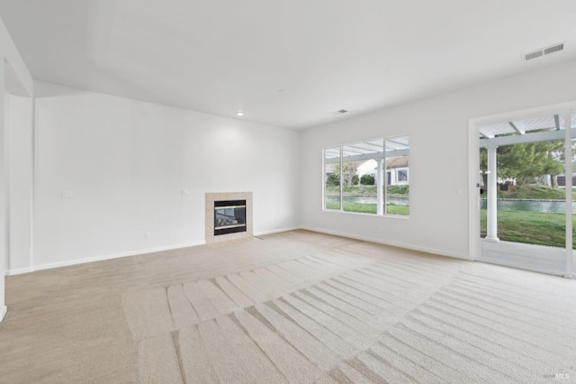unfurnished living room featuring a tiled fireplace and light colored carpet