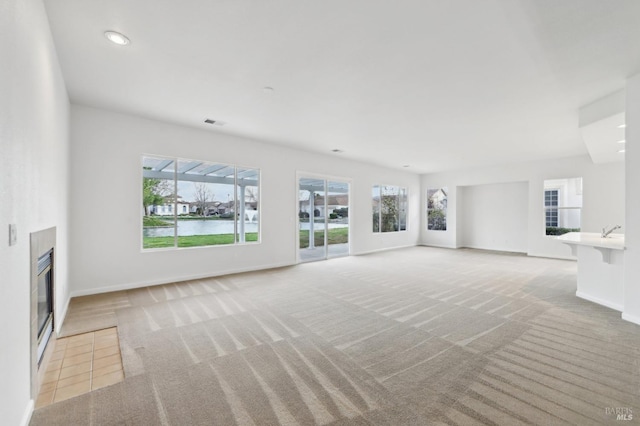 unfurnished living room featuring a healthy amount of sunlight, light colored carpet, and a tiled fireplace