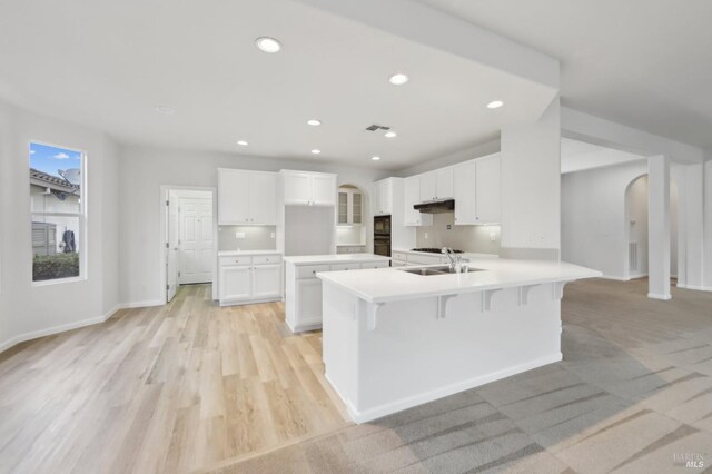 kitchen featuring light wood-type flooring, white cabinets, a breakfast bar, sink, and kitchen peninsula