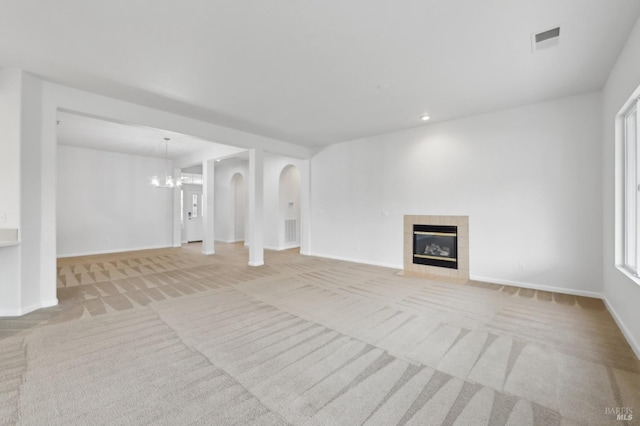 unfurnished living room with a tiled fireplace, light colored carpet, and an inviting chandelier
