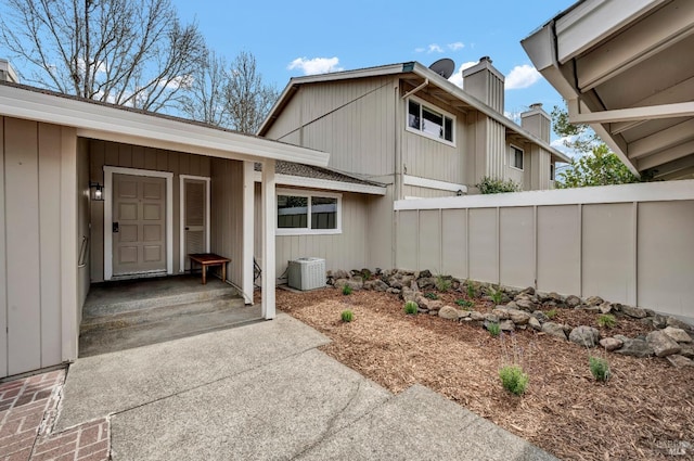 entrance to property with a chimney, fence, and cooling unit