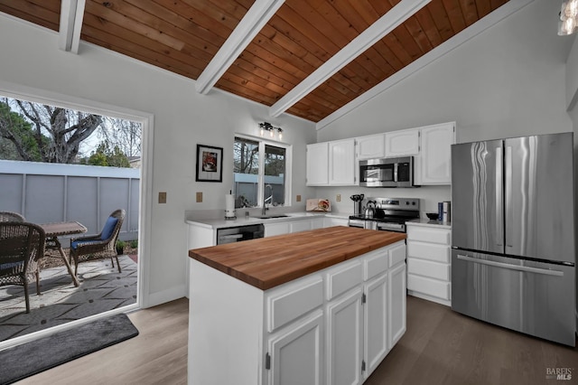 kitchen with butcher block countertops, wood finished floors, white cabinetry, appliances with stainless steel finishes, and vaulted ceiling with beams