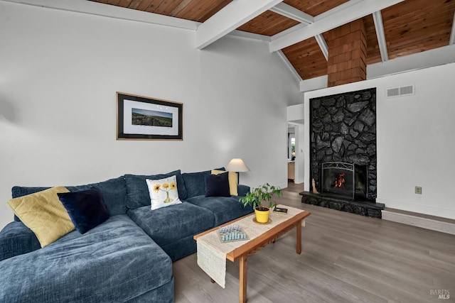 living room with visible vents, wood finished floors, a stone fireplace, wood ceiling, and vaulted ceiling with beams