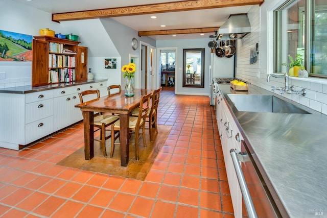 kitchen with tile patterned floors, beamed ceiling, a sink, stainless steel counters, and decorative backsplash