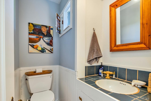 half bath featuring wainscoting, toilet, and vanity