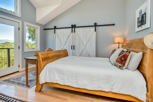 bedroom featuring access to exterior, lofted ceiling, a barn door, and wood finished floors