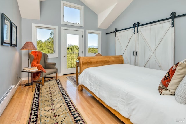 bedroom with multiple windows, access to outside, a barn door, light wood finished floors, and baseboard heating