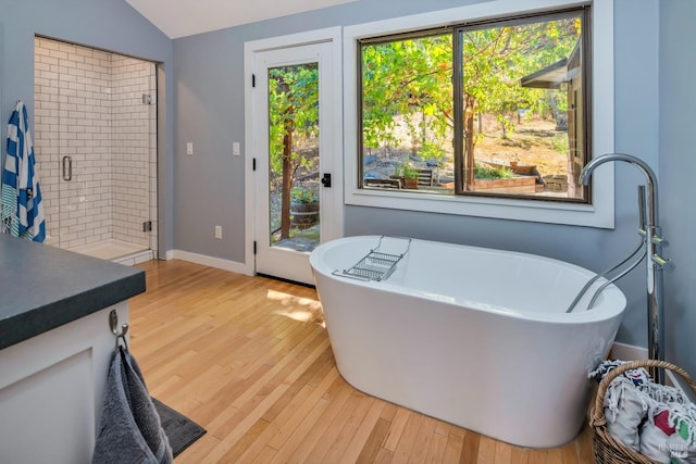 bathroom featuring vaulted ceiling, plenty of natural light, a freestanding tub, and wood finished floors