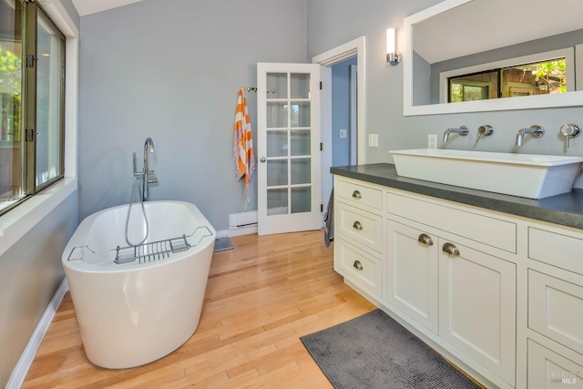 full bathroom featuring vanity, wood finished floors, baseboards, a baseboard radiator, and a freestanding tub