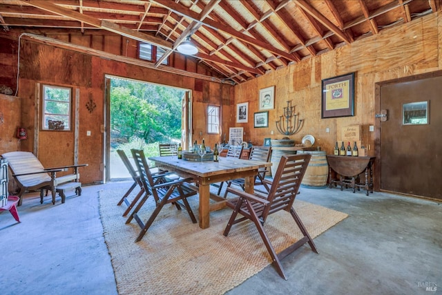 dining space with wooden walls, concrete floors, and high vaulted ceiling