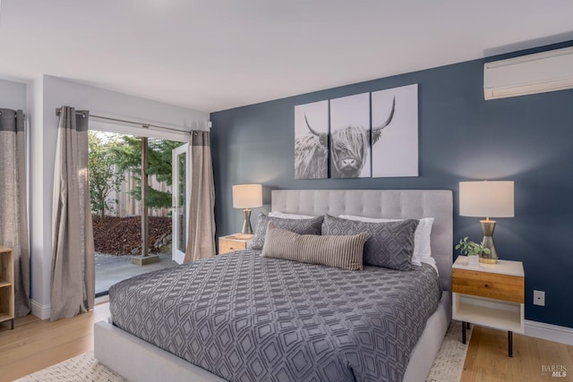 bedroom featuring access to exterior, an AC wall unit, baseboards, and wood finished floors