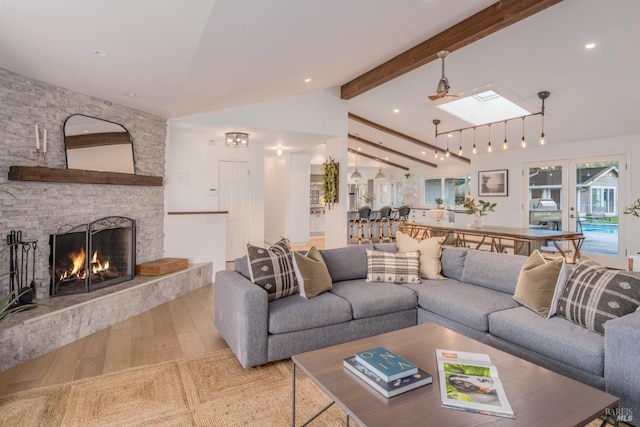 living area featuring lofted ceiling with skylight, recessed lighting, wood finished floors, and a stone fireplace