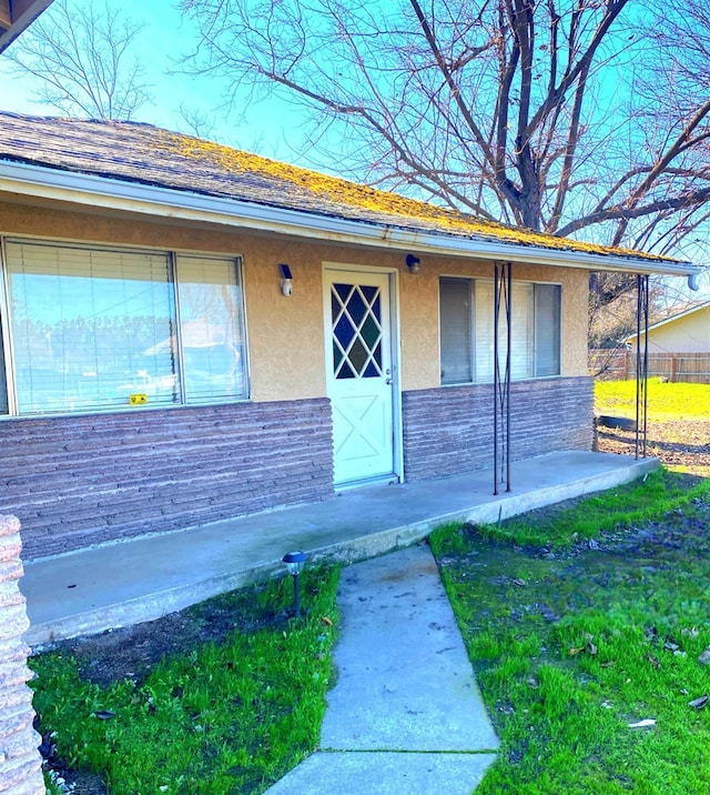 entrance to property featuring stone siding, a yard, and stucco siding