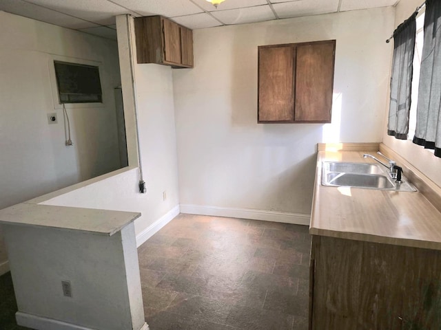 kitchen featuring brown cabinets, a paneled ceiling, light countertops, a sink, and baseboards