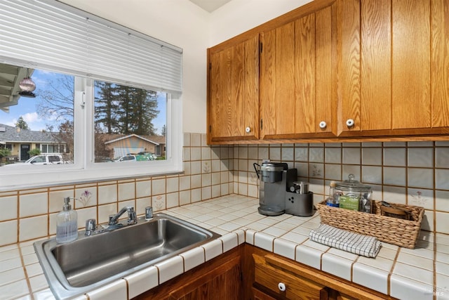 kitchen featuring decorative backsplash, tile counters, brown cabinetry, and a sink