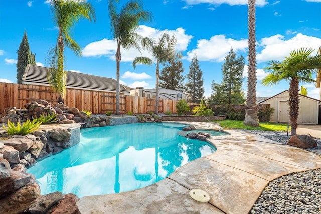 view of pool featuring an outbuilding, a storage unit, a fenced backyard, and a pool with connected hot tub