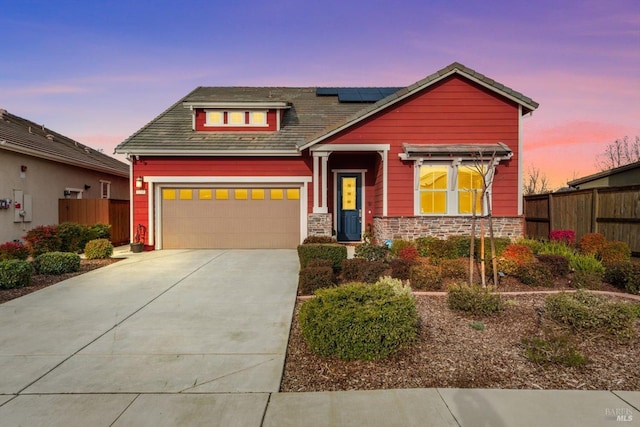 craftsman house with a garage, solar panels, concrete driveway, stone siding, and fence