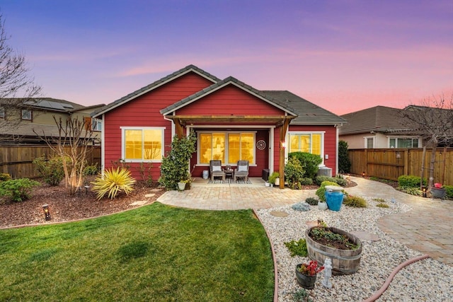 back of house at dusk with a patio area, a fenced backyard, and a lawn