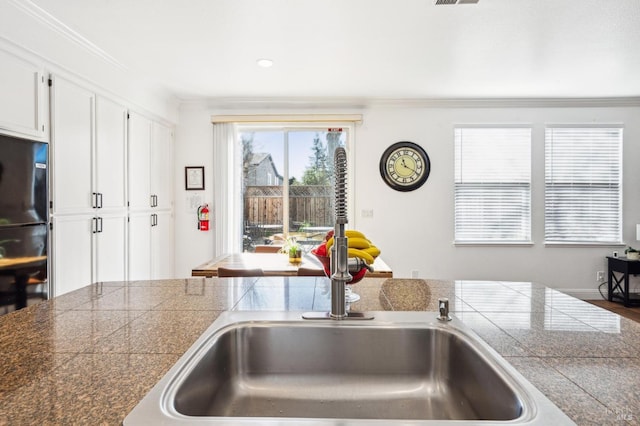 kitchen featuring visible vents, tile countertops, crown molding, white cabinetry, and a sink