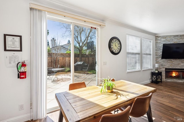 dining space featuring ornamental molding, a stone fireplace, baseboards, and wood finished floors