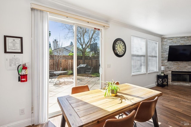 dining area featuring baseboards, a stone fireplace, wood finished floors, and crown molding