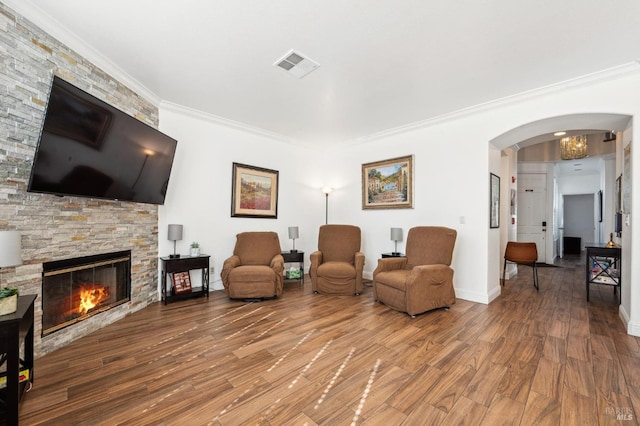 sitting room featuring visible vents, arched walkways, wood finished floors, crown molding, and a stone fireplace