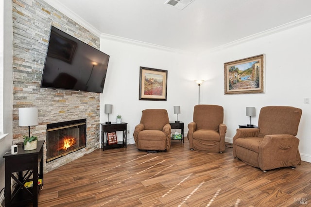 living area featuring baseboards, visible vents, wood finished floors, crown molding, and a fireplace