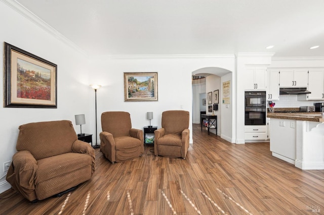 living area featuring ornamental molding, arched walkways, light wood-type flooring, and baseboards