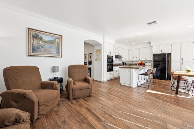 living room with light wood-type flooring, visible vents, arched walkways, and ornamental molding