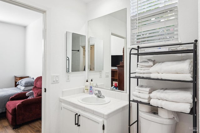 bathroom featuring toilet, ensuite bath, wood finished floors, and vanity