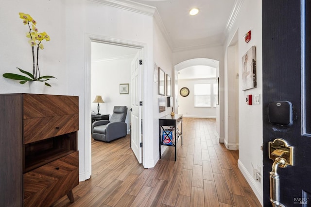 hallway featuring arched walkways, crown molding, baseboards, and wood finished floors